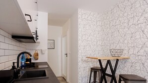 A modern kitchen with a black countertop, a sink, and a wooden table with two stools. - Toruń Studzienna Cozy Urban Studio (Toruń)