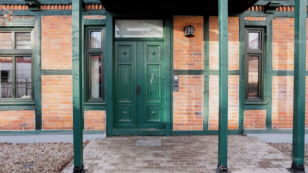 A building with a green door and windows, brick walls, and a covered entrance area. - Toruń Studzienna Cozy Urban Studio (Toruń)