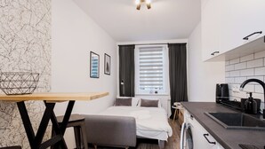 A compact hotel room with a bed, a small kitchenette, a washing machine, and a dining area with a table and chairs. - Toruń Studzienna Cozy Urban Studio (Toruń)
