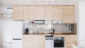 A modern kitchen with wooden cabinets, a built-in dishwasher, a microwave, and a coffee maker. - Lubicka 69 Urban Retreat Apartment (Toruń)