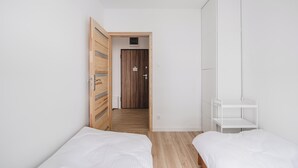 A bedroom with two beds, a wooden wardrobe, and a white shelving unit. - Lubicka 69 Urban Retreat Apartment (Toruń)