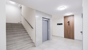 A clean, modern interior with a staircase, an elevator, and a wooden door marked with the number 1. - Lubicka 69 Urban Retreat Apartment (Toruń)