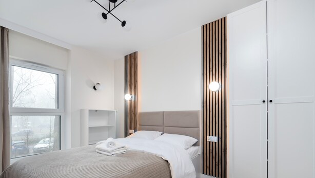 Camera moderna con un letto grande, parete rivestita in legno, armadio bianco e finestra con vista su auto parcheggiate.