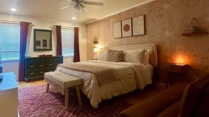 Ein Schlafzimmer mit einem Bett, Nachttischen, einem Schreibtisch, einem Stuhl, einem Deckenventilator und einem gemusterten Teppich.