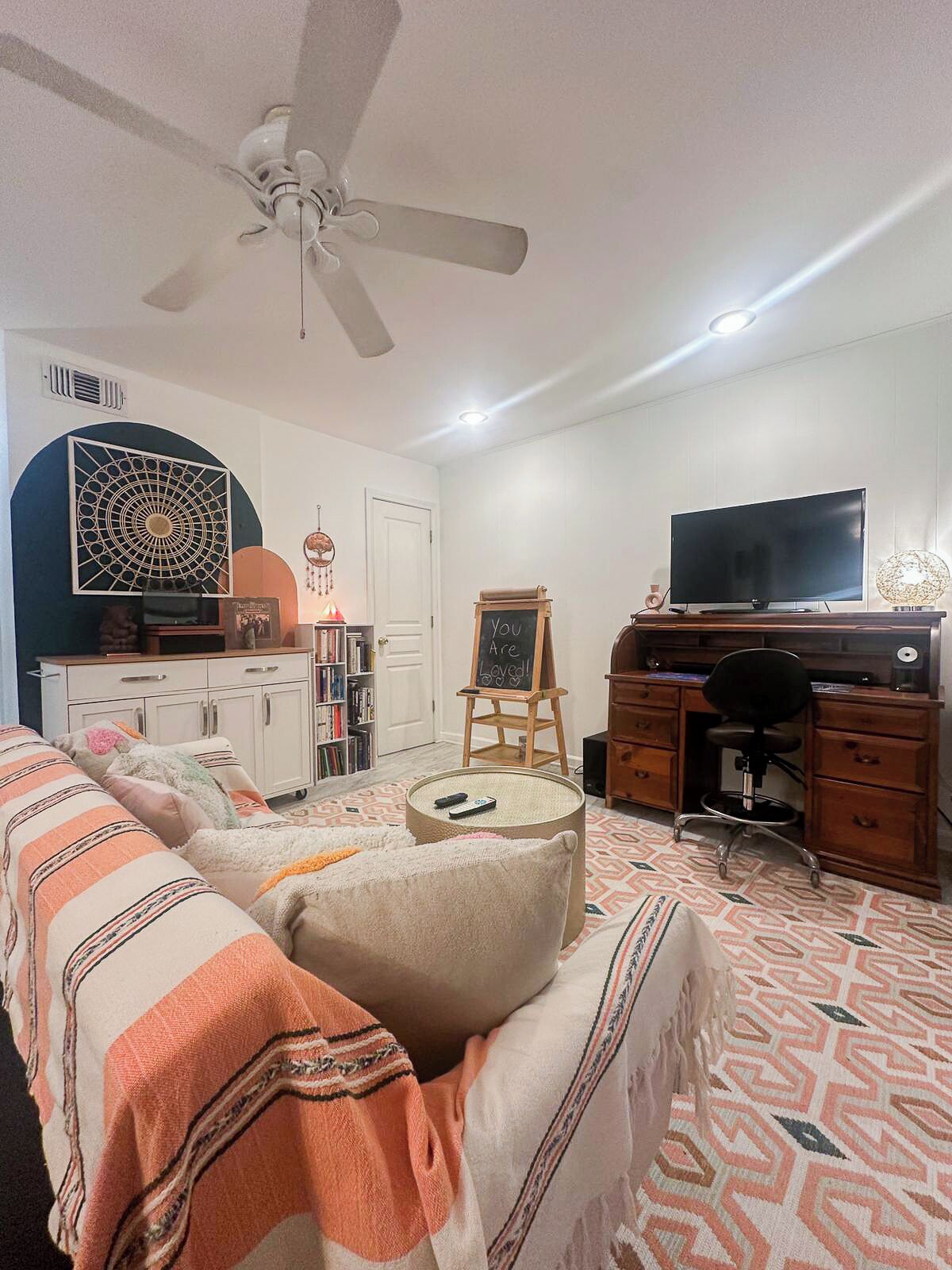 A living room with a sofa, a desk, a television, and a ceiling fan.