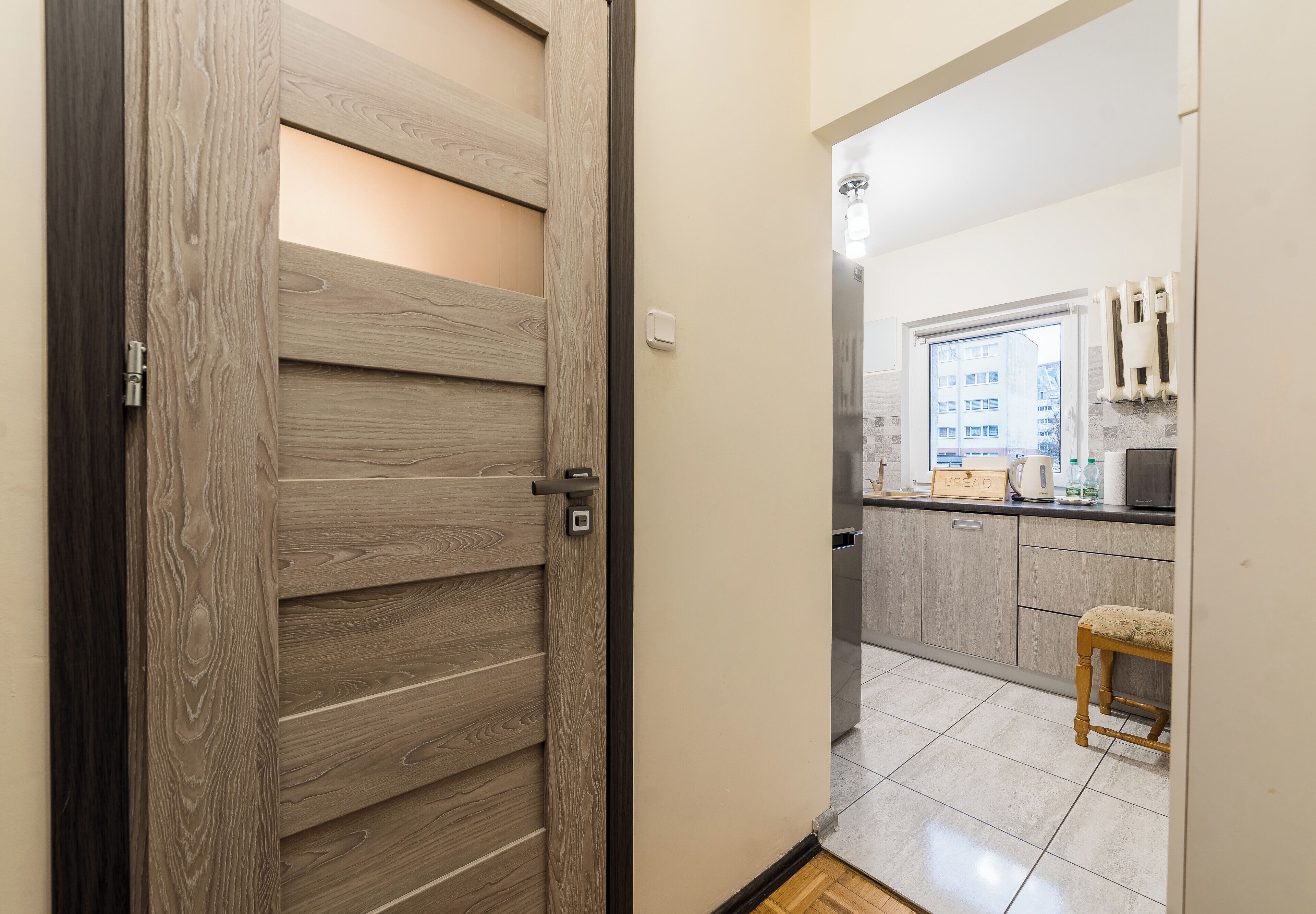 Una porta in legno che dà su una cucina con uno sgabello e vista su un edificio esterno.