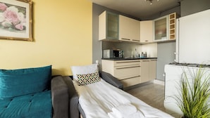 Ett kompakt bostadsutrymme med en soffa, en säng, ett litet kök och en krukväxt.