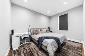 Ein modernes Schlafzimmer mit Bett, Schreibtisch, Stuhl und einem großen Fenster.