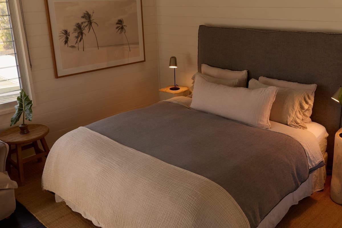 Een slaapkamer met een groot bed, een nachtkastje met lamp, een lijst met afbeelding en een bloempot.