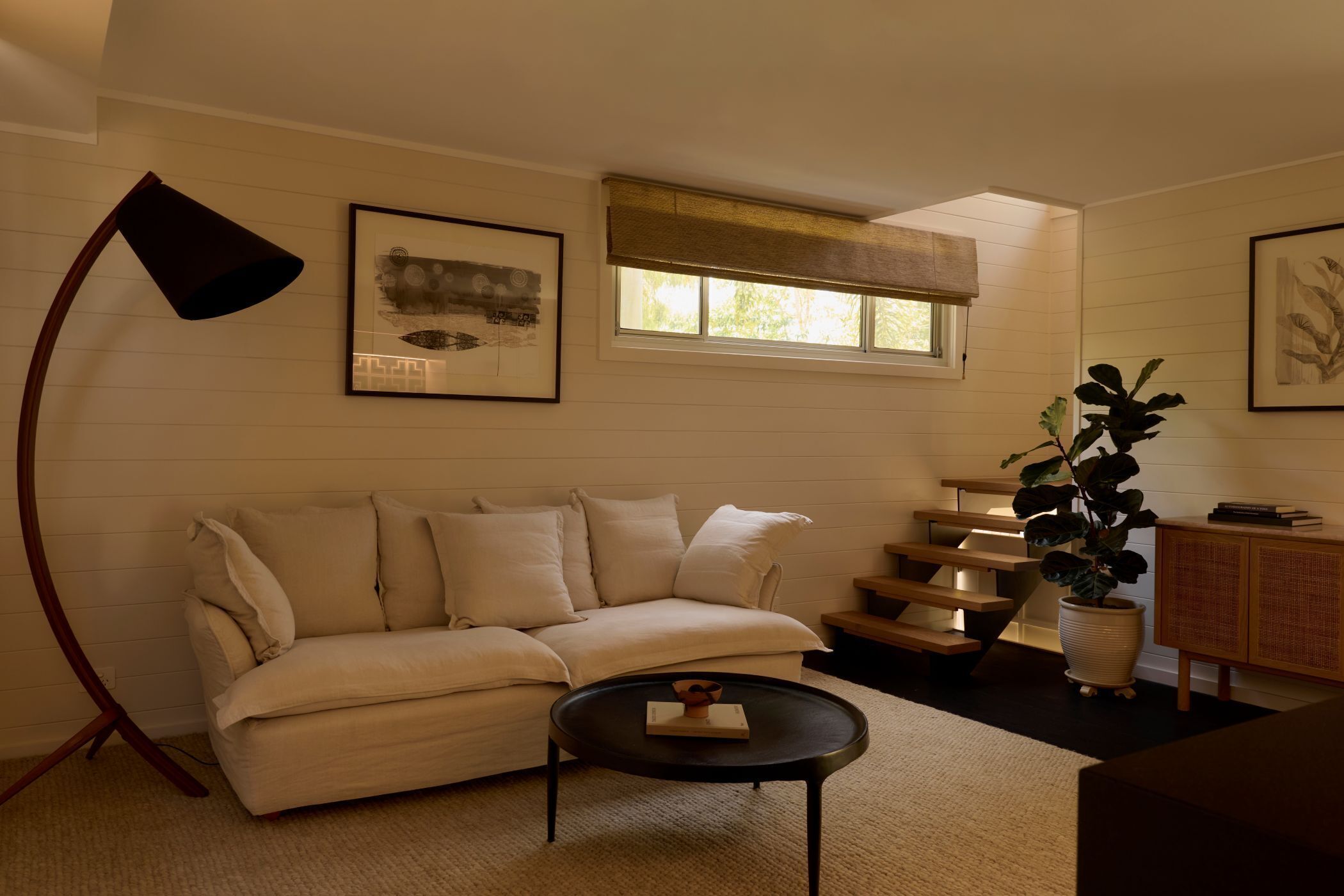 A living room with a sofa, a coffee table, a lamp, a plant, and artwork on the walls.