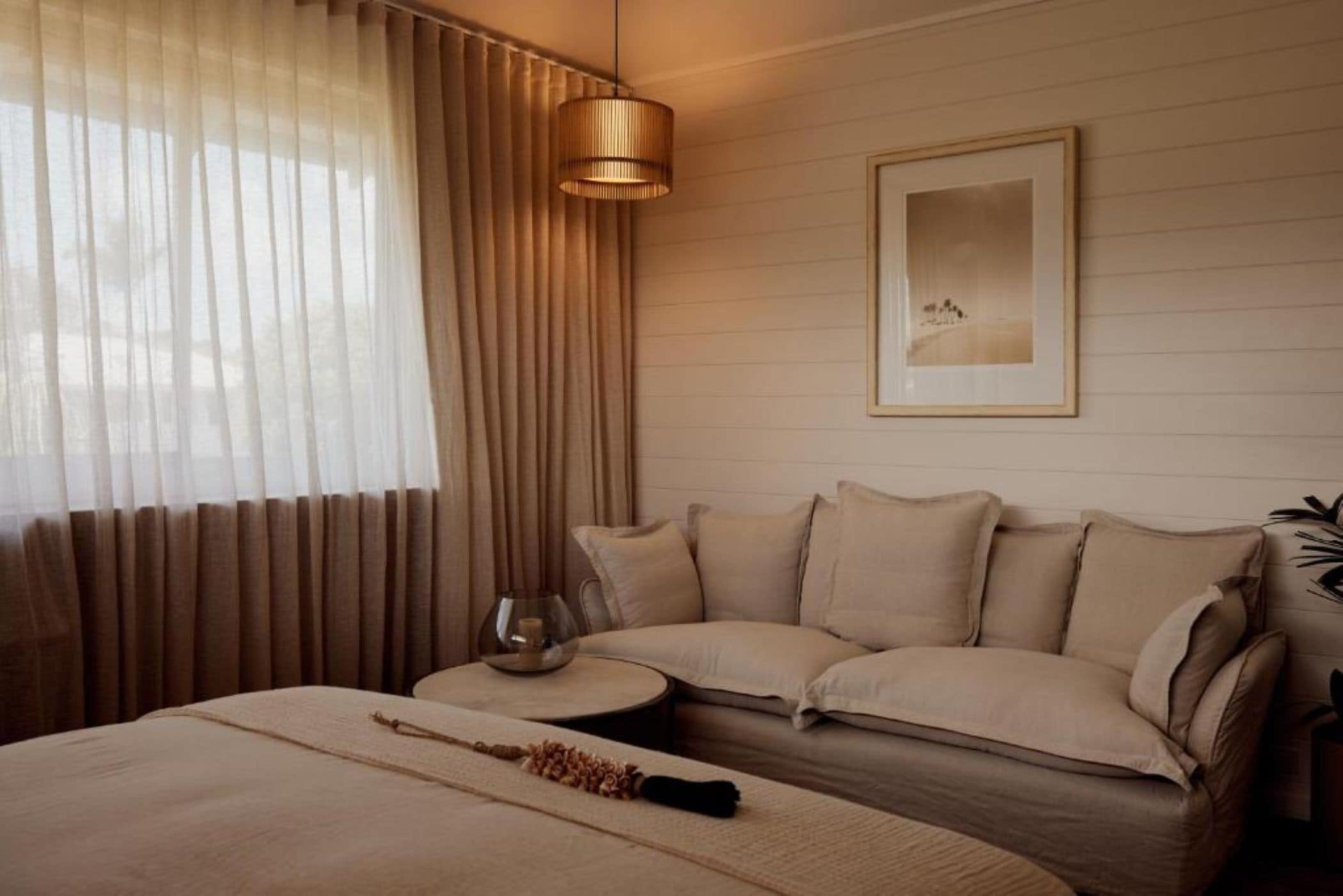 A modern bedroom with a large bed, a sofa, a round coffee table, and a pendant light.