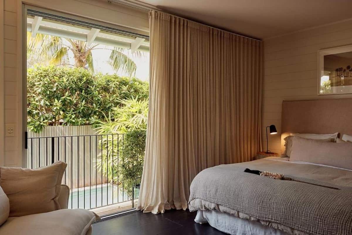 Een slaapkamer met een groot bed, een balkon met gordijnen en uitzicht op groen.