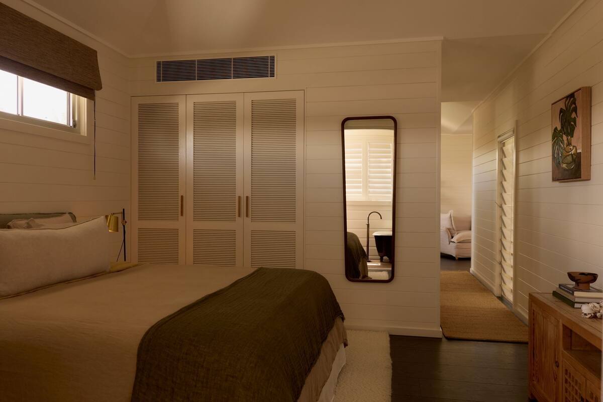 Een slaapkamer met een bed, een spiegel, een kledingkast, en een zichtbare badkamer door een open deur.