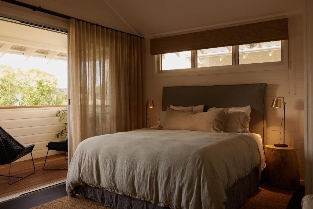 A bedroom with a large bed, a window with curtains, a bedside table with a lamp, and a chair by the window.