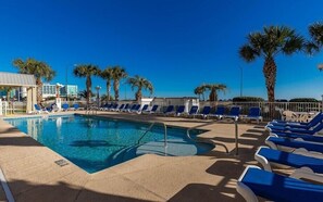 A pool area with clear blue water, surrounded by blue lounge chairs and palm trees. - Gorgeous Ocean View - Grande Caribbean Orange Beach 2 BR Condo (Orange Beach)