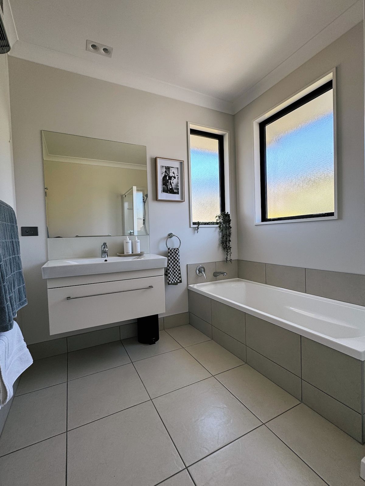 A modern bathroom with a large mirror, a bathtub, and a window.
