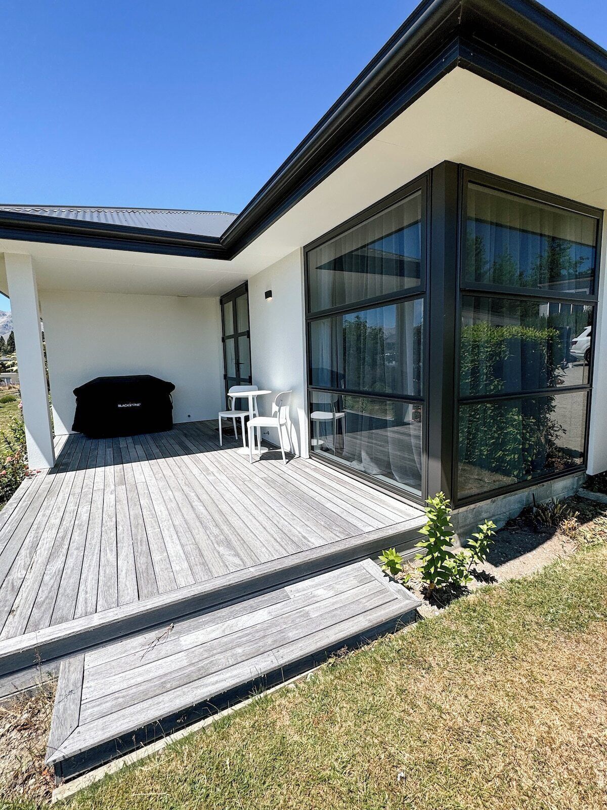 A modern house with a wooden deck, a barbecue area, and a glass-enclosed patio.