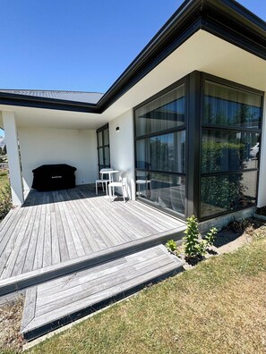 Ein modernes Haus mit einer Holzdiele, einem Grillplatz und einer gläsernen Veranda.