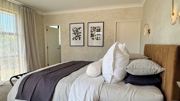 A bedroom with a large bed, a bedside table, a headboard, and two framed pictures on the wall.
