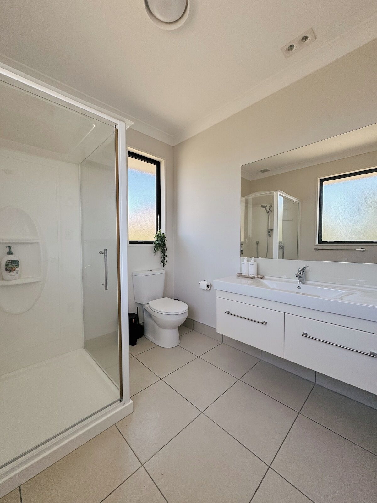 A modern bathroom with a glass-enclosed shower, a toilet, and a vanity with a mirror.