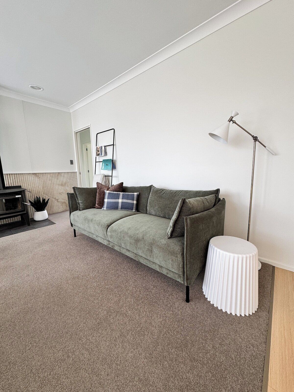 A living room with a sofa, a small white side table, a floor lamp, and a bookshelf.