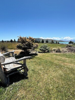 Un banco de madera rústico en un campo cubierto de hierba, con una montaña y un lago al fondo.