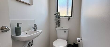 A small, clean bathroom with a white sink, toilet, and a window with a view.