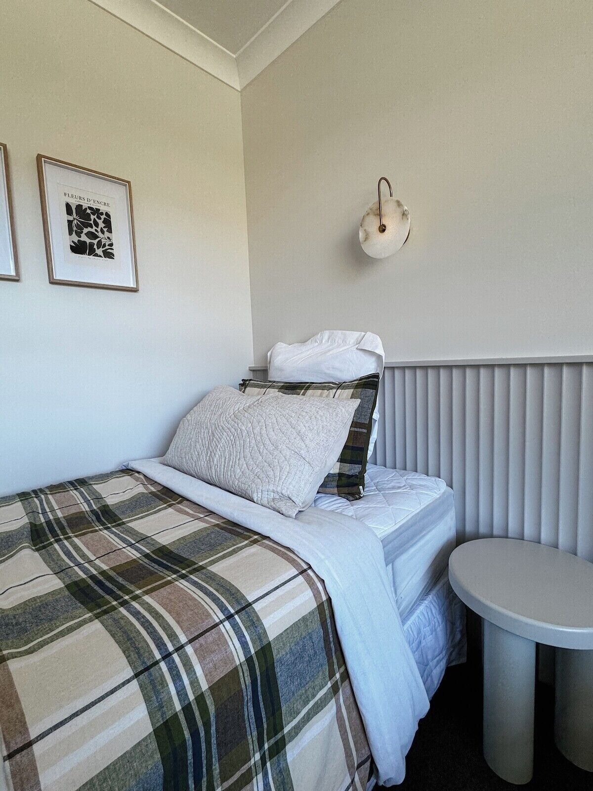 A bedroom with a bed, a round table, and a wall-mounted light fixture.