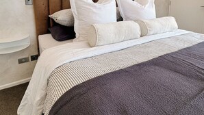 Habitación de hotel con cama, almohadas, cabecera, apliques de pared, una puerta y un estante pequeño.