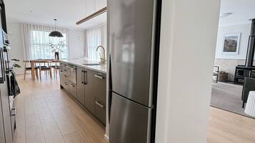 A modern kitchen with a stainless steel refrigerator, wooden cabinets, and a dining area with a table and chairs.