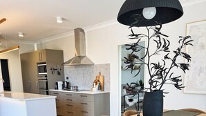 Una cocina moderna con una isla central, una zona de comedor con mesa y sillas de madera, y una lámpara colgante negra.