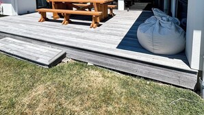 Una casa moderna con un patio que incluye una mesa de madera y bancos, un sillón inflable grande y un techo con paneles solares.