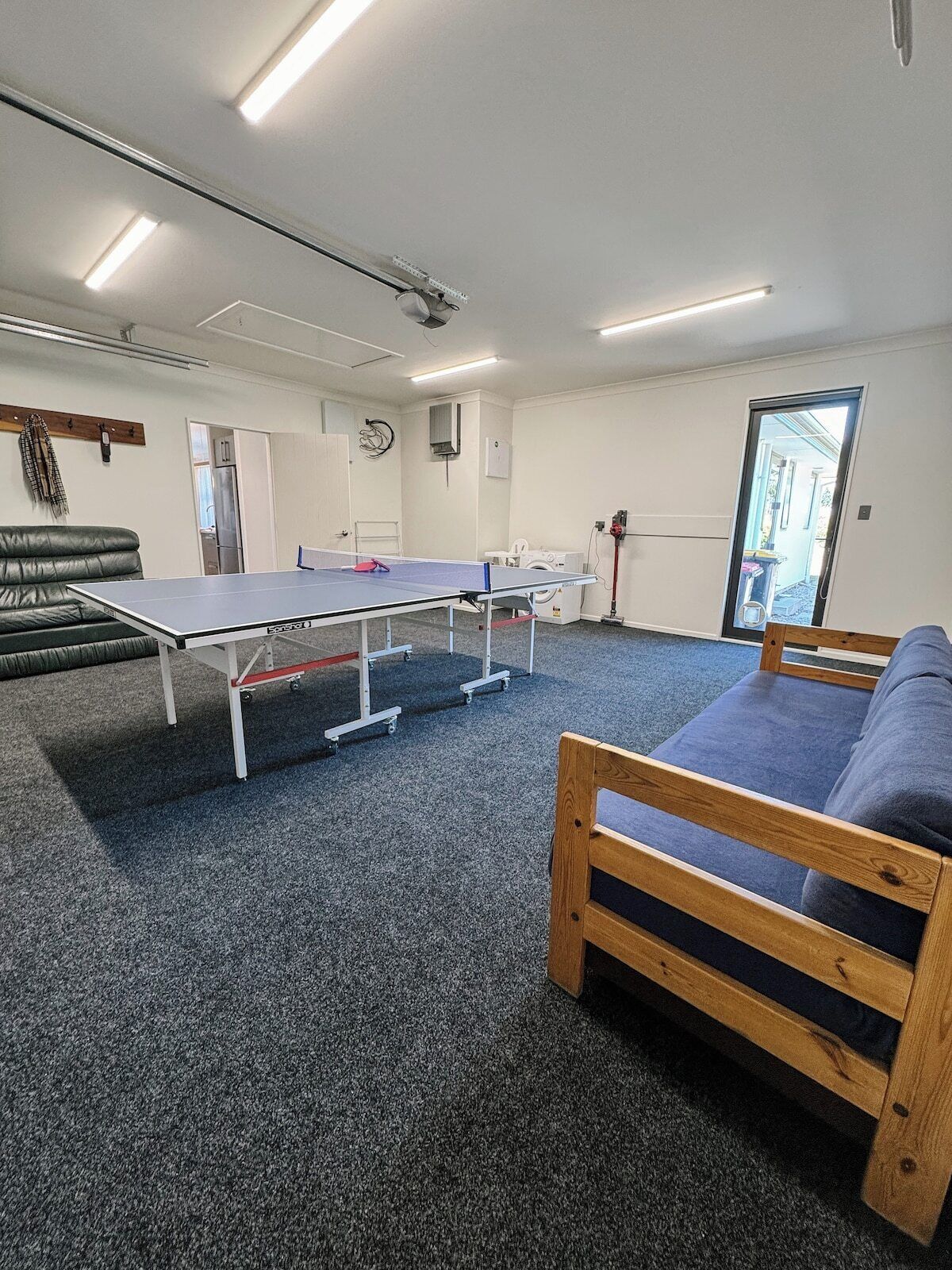 Ein Zimmer mit Tischtennisplatte, einer Couch, einer Waschmaschine und einer Tür zu einem Außenbereich.
