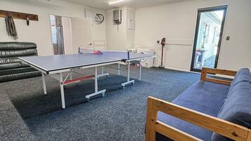 Ein Zimmer mit Tischtennisplatte, einer Couch, einer Waschmaschine und einer Tür zu einem Außenbereich.