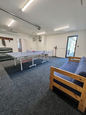 Ein Zimmer mit Tischtennisplatte, einer Couch, einer Waschmaschine und einer Tür zu einem Außenbereich.