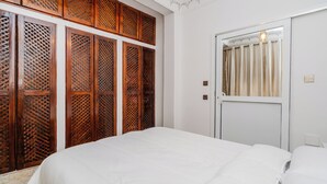 Un dormitorio con cama, un separador de madera, una puerta blanca con ventanal y una lámpara.