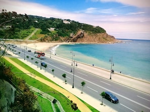 Eine Küstenstraße mit einem Strand auf der einen Seite und einer hügeligen Landschaft mit Gebäuden auf der anderen.