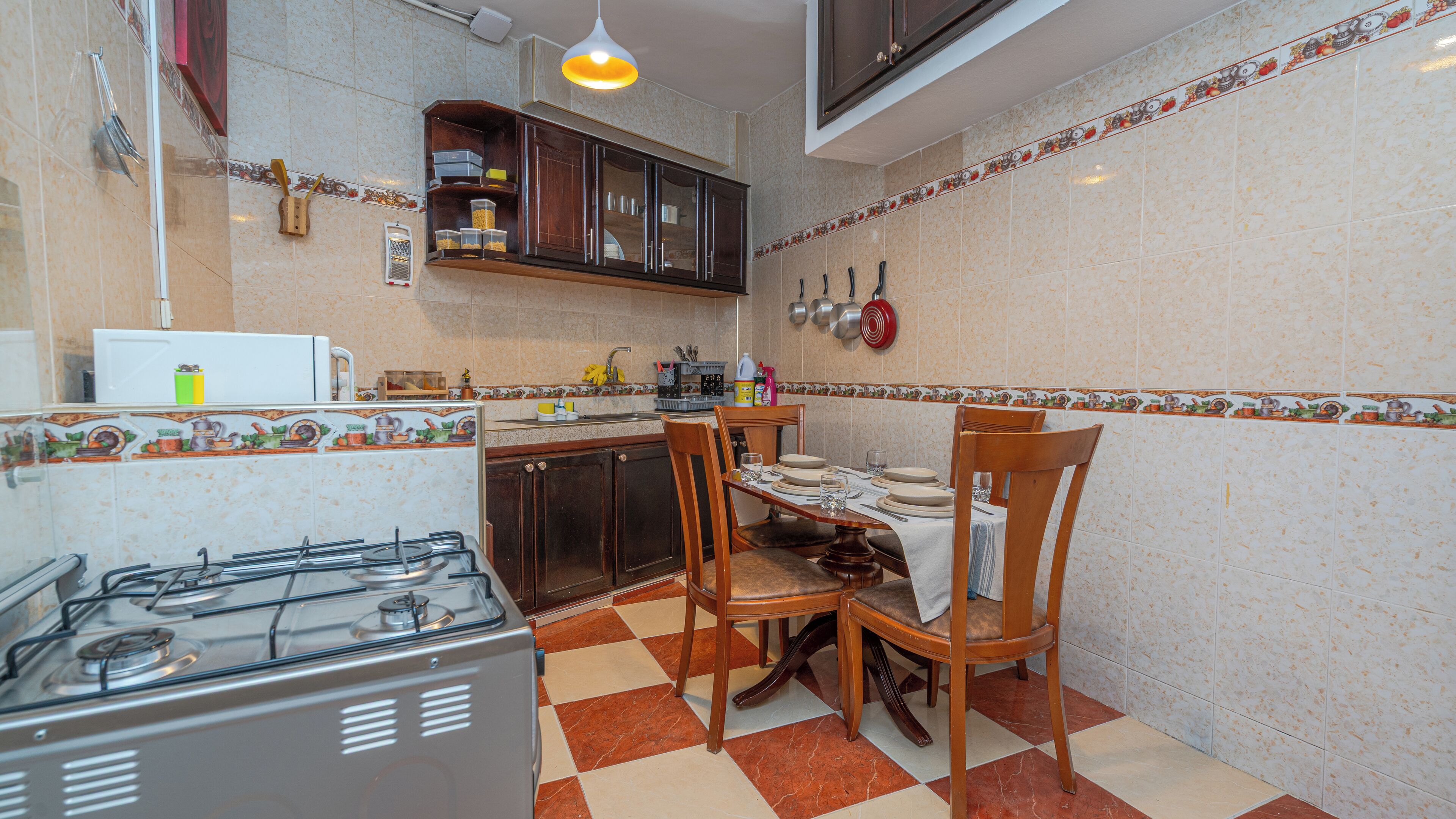 A compact kitchen with a gas stove, wooden chairs, a dining table, and a microwave.