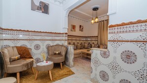 Una sala de estar con sofá, sillones, una mesa de centro y baldosas con diseño en las paredes.