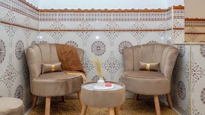 Una habitación con dos sillones cómodos, una mesita redonda con un jarrón y una flor, y un papel tapiz estampado.