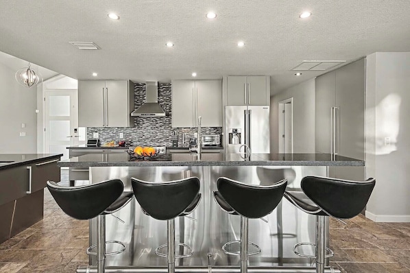 Una cocina moderna con una isla central, electrodomésticos de acero inoxidable y taburetes negros.