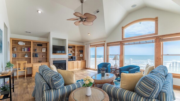 A spacious living area with a large sofa set, a television, a fireplace, and a view of the ocean. - Oceanfront Oasis w/ Elevator, Pool, Hot Tub, Pool Table, Pets OK, Flex Stays (Nags Head)