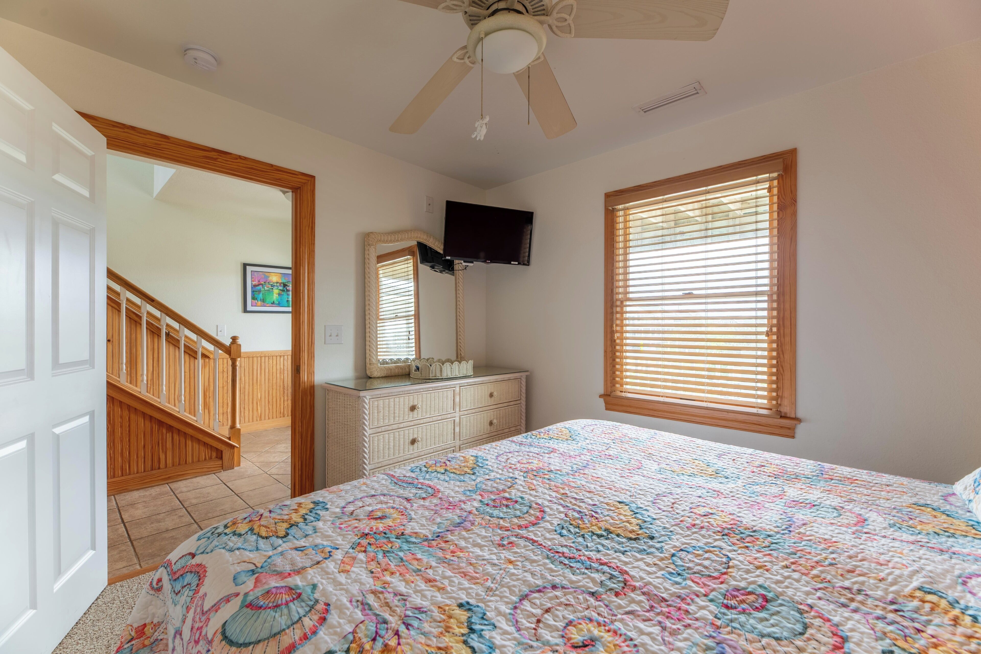 A bedroom with a bed, dresser, TV, and a ceiling fan.