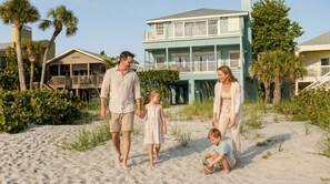 Eine Familie am Sandstrand, im Hintergrund ein zweigeschossiges Gebäude.