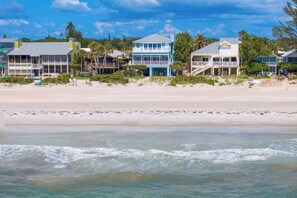 Ein direkt am Strand gelegenes Anwesen mit mehreren Gebäuden, darunter ein zweistöckiges Haus mit Balkon und ein kleineres Gebäude mit Veranda.