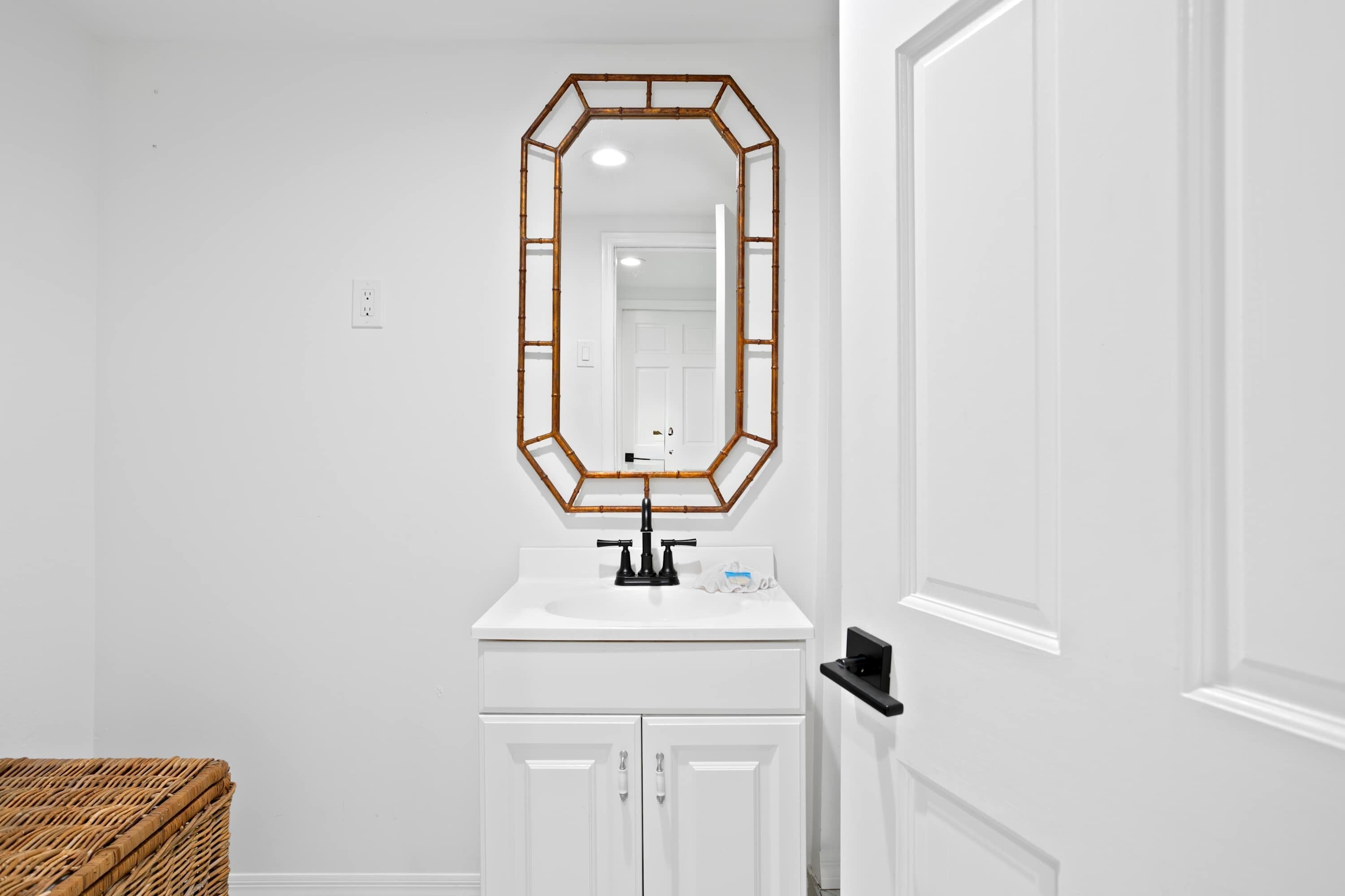 Un bagno con un mobile lavabo bianco, uno specchio con cornice geometrica e un cesto di vimini.