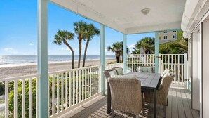 A covered outdoor area with a table and chairs, overlooking a beach with palm trees and the ocean. - Walks on the Shores • Private Beach Front Access (Indian Shores)