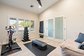 Ein Zimmer mit einem Ergometer, einem Sandsack, einer Bank und einem Bett mit Kissen.