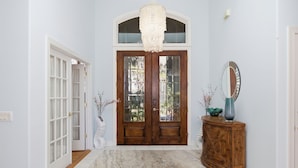 A hallway with a wooden double door, a chandelier, a mirror, and a cabinet. - Beautiful Palmetto Dunes home with bikes, pool, hot tub. (Hilton Head Island)