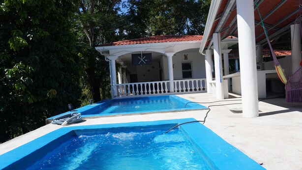 A pool area with two rectangular pools, a covered seating area, and a clock on the wall.
